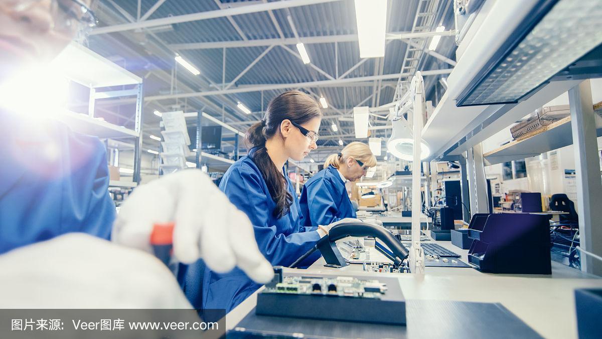 女電子工廠的工人在藍(lán)色的工作外套和保護(hù)眼鏡組裝筆記本電腦的主板與